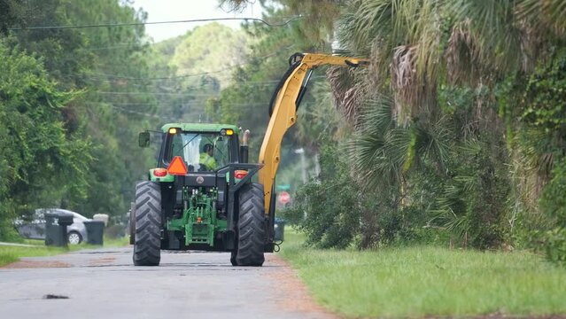 Public works utility tractor pruning trees and greenery braches on Florida rural street side