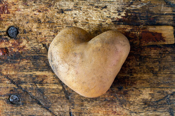 Potato tuber in the form of a heart against the background of old wood. Potato tuber close-up.