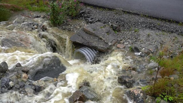 Rainwater rushes into culvert running under road during flooding in Norway.