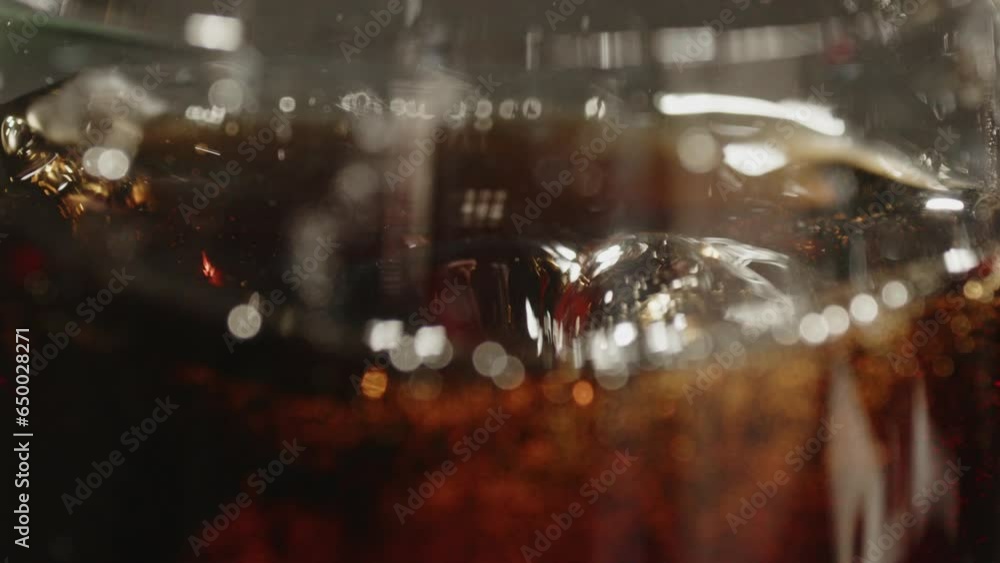 Poster macro shot of ice cubes falling in a glass of cola in slow motion