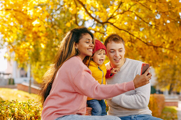 A happy family with a smiling child takes a selfie with autumn leaves