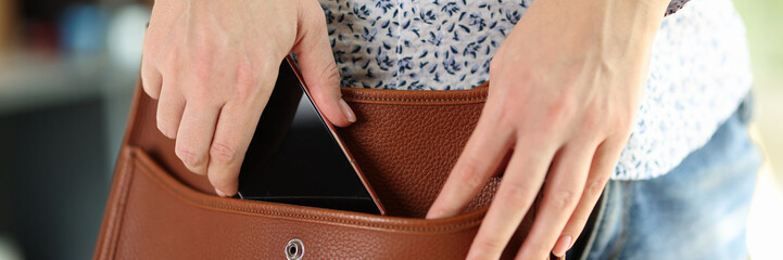 Woman in casual clothes holds her smartphone in her shoulder bag.