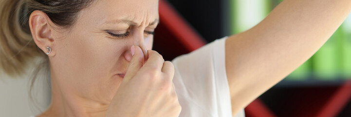 Sad woman closes her nose while looking at her armpit close-up.