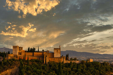 The Alcazaba of the Alhambra in Granada, Spain, illuminated by the warm light of sunset, with a beautiful sky in orange and blue tones in the background