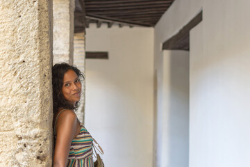 A beautiful woman with curly hair leaning against an ancient stone column inside an ancient...