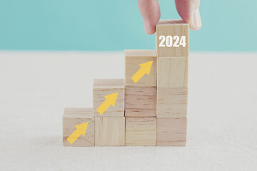 Hand holding 2024 and arrows ladder up on wooden blocks, growth and success business concept