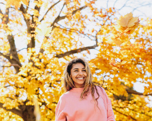 A charmingly wide smiling African-American girl who playfully tosses autumn maple leaves up.