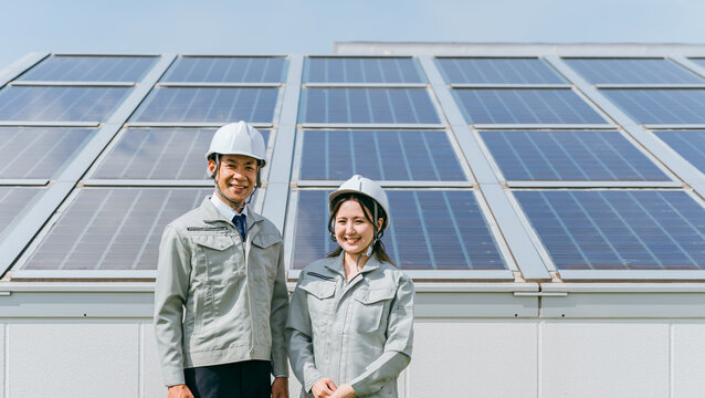太陽光発電・ソーラーパネルの前に立つ電力会社・電気工事業者の作業着姿の技術者・ビジネスパーソン
