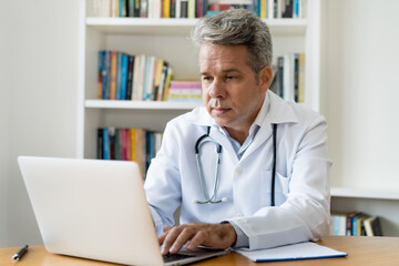 Älterer Arzt schaut in die digitale Patientenakte - obrazy, fototapety, plakaty