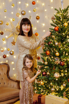 Mother and daughter in golden dresses decorated christmas tree