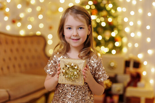 Happy little girl in golden dress holding christmas gift box in hands