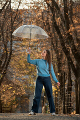 Happy young woman with long hair walks in autumn park. Beautiful girl with transparent umbrella
