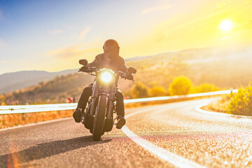 Sunset over an open road and a man with a helmet riding a motorbike