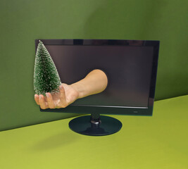 A woman's hand comes out of a computer monitor and holds a Christmas tree. Green background.