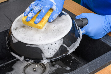 Mycie dna patelni gąbką w zlewie z dużą ilością płynu do naczyń 