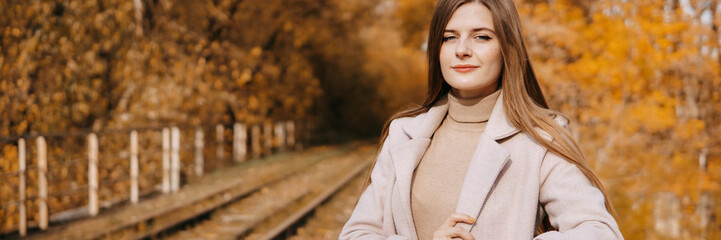 beautiful long-haired woman walks through the autumn streets. Railway, autumn, woman in a coat.