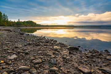 Golden dawn on the sandy, pebbly riverbank, clouds in the distance, fog, reflection in the water. - 650083437