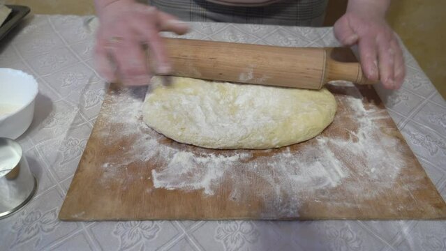a woman rolls out the dough with a rolling pin,a woman is rolling out the dough on the table