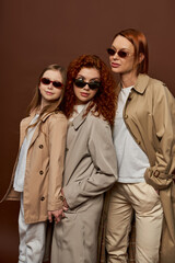 Fototapeta premium three female generations with red hair posing in sunglasses and coats on brown backdrop, family bond