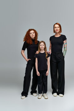 family photo, three generations of women in matching navy blue attire standing on grey background