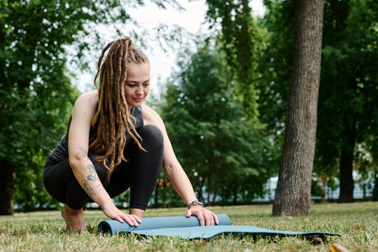 Young woman preparing exercise mat for practice outdoors
