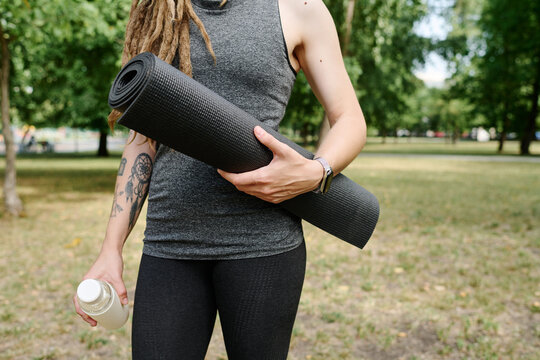 Close-up of young healthy woman standing with exercise mat outdoors after sport training