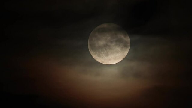 Full moon on a dark cloudy night with colored and black clouds flying in front of the moon in the sky, like in thrillers and horror films. Real shooting