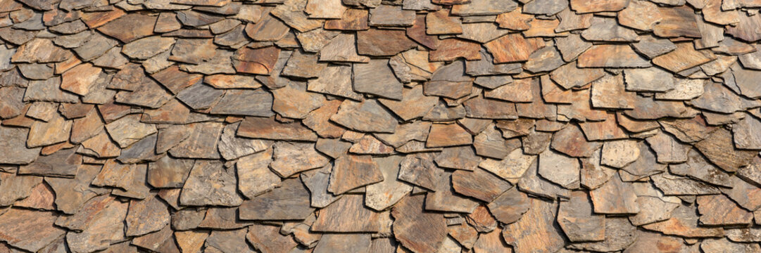 Closeup of natural brown stone shingle slate tiles. Texture roof surface background. Panoramic image