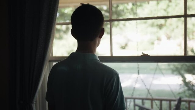 Young man, teenage boy looking outside window.