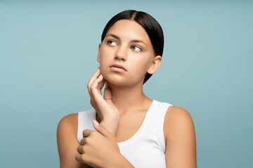 Pensive brunette shy teen girl thinking looking aside isolated on studio blue background. Beauty,...
