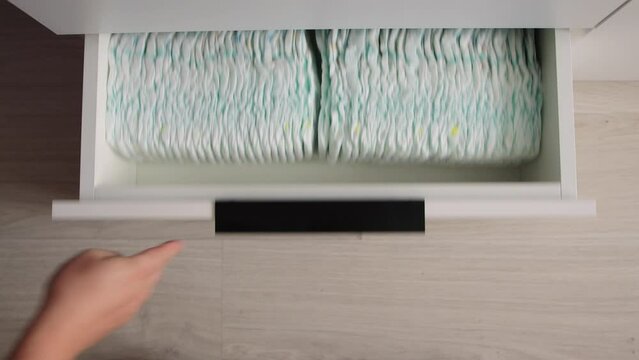 The man opened the chest of drawers with baby diapers, took the diapers and closed the chest of drawers. Cotsnept protection against leakage of children, hypoallergenic diapers, hygiene. Close-up