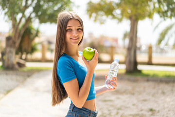 Teenager girl at outdoors with an apple and with a bottle of water