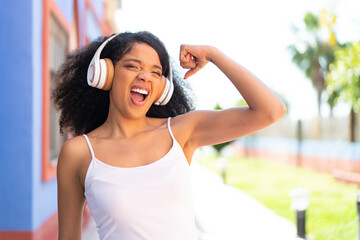 Young African American woman with headphones at outdoors doing strong gesture