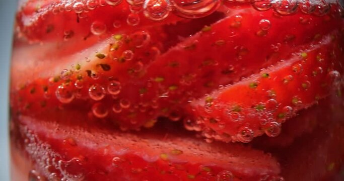 Closeup of strawberries in glass of water with bubbles. Appetizing strawberry cocktail in glass with drops of wet water and soda