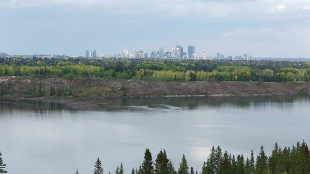 An aerial drone flies towards the City of Calgary over the tree lined Glenmore reservoir during autumn