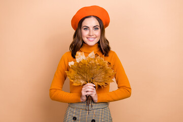 Photo of positive nice girl beaming smile hands hold bunch fallen leaves isolated on beige color...