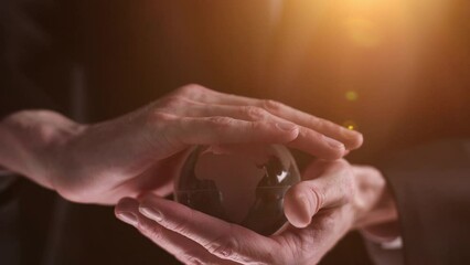 Hands holding a transparent crystal glass ball on a black background