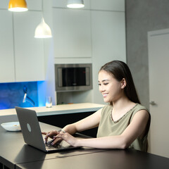 Work from home. Asian girl working on a laptop in the kitchen. Square photography.