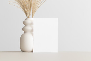 White invitation card mockup with a reed pampas decoration on the beige table. 5x7 ratio, similar to A6, A5.