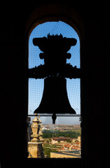 Obraz premium Backlit silhouette of the bronze bell of the old cathedral with the view of the city and mountains of Salamanca from the church tower. Protected with an anti-pigeon mesh.