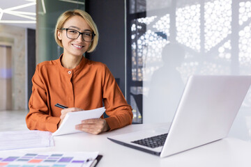 Portrait businesswoman at the workplace with a notebook in hands, a female employee smiling looking at the camera, a woman increases her knowledge, watches a video course, web seminar, webinar.