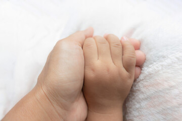 Child's hand holding mother's hand on soft, light pink cloth. soft focus.