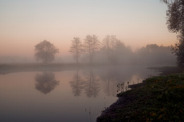 Autumn foggy landscape over the lake at dawn.