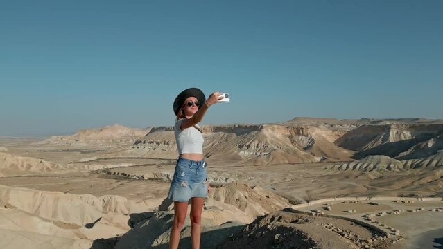 European woman wearing casual clothes taking selfie, the Negev Desert in Israel is visible in the background over mountains, sandy hills and rock formations.
Near David and Paula Ben Gurion gravesite.