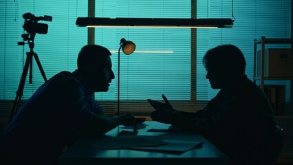 Medium silhouette shot of an offender, perpetrator or prisoner sitting in the interrogation room in...