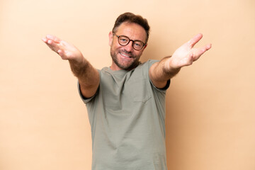 Fototapeta premium Middle age caucasian man isolated on beige background presenting and inviting to come with hand