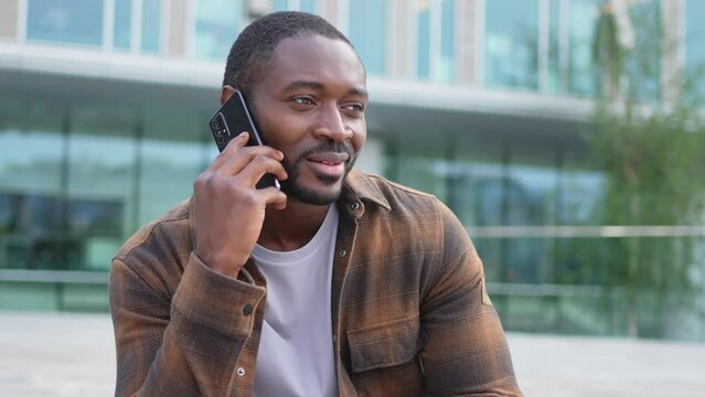 African american man talking on smartphone on street in city outdoor. Man with cell phone chatting with friends. Smiling person making answering call by cellphone. Guy having conversation by mobile