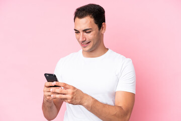 Young caucasian man isolated on pink background sending a message or email with the mobile
