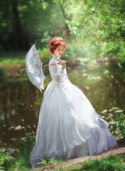 Fototapeta na wymiar Beautiful red haired girl in white long vintage dress and lace umbrella standing near river.Pretty tenderness model with perfect wedding hairstyle dreaming.Art work and fairy tale