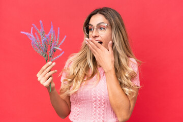 Young pretty Uruguayan woman holding lavender isolated on red background with surprise and shocked...